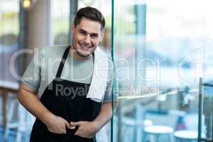 Smiling waiter leaning on glass door in cafÃ?Â©