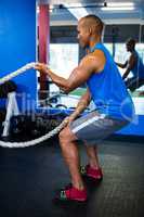 Male athlete exercising with ropes in gym