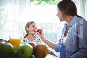 Mother feeding apple to her daughter while having breakfast