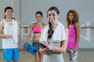 Portrait of female trainer holding clipboard with fitness class in background