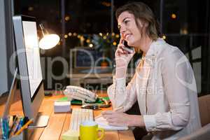Businesswoman talking on mobile phone while working on computer at her desk