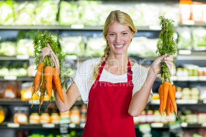 Smiling female staff holding bunch of carrots in organic section