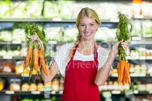 Smiling female staff holding bunch of carrots in organic section