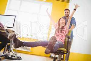 Portrait of businessman pushing cheerful colleague sitting in chair at creative office