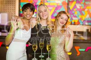 Three smiling female friends standing with arm around in bar