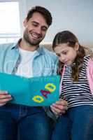 Father and daughter reading greeting card while relaxing on sofa