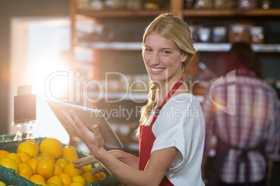 Smiling staff using digital tablet while checking fruits in organic section