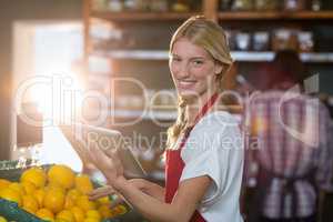Smiling staff using digital tablet while checking fruits in organic section