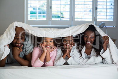 Happy family lying under a blanket on bed