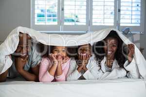 Happy family lying under a blanket on bed