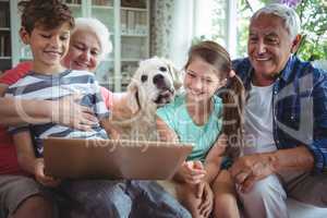 Grandparents and grandchildren using laptop in living room