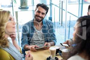 Friends using mobile phone and digital tablet while having cup of coffee