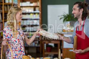 Smiling male staff giving loaf of bread to woman