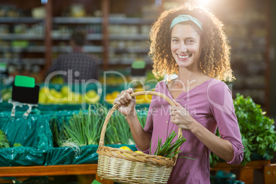 Smiling woman holding basket of vegetables in organic section