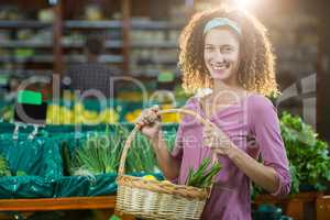 Smiling woman holding basket of vegetables in organic section