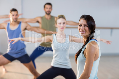 Instructor smiling at camera while students performing stretching exercise