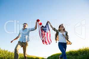Couple holding amrican flag and running in field
