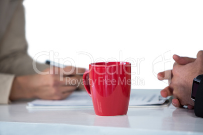 Businesswomen writing on clipboard with coffee mug on desk