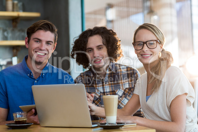 Smiling friends using digital tablet and laptop in cafÃ?Â©