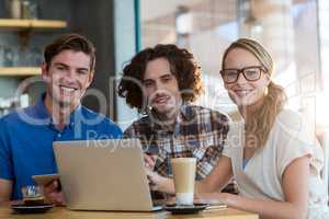 Smiling friends using digital tablet and laptop in cafÃ?Â©