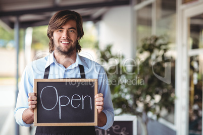 Portrait of waiter showing chalkboard with open sign