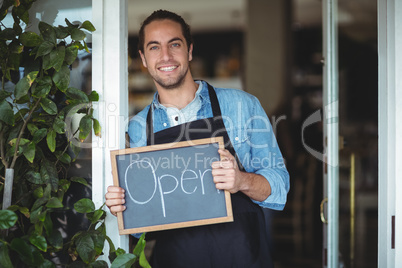 Portrait of smiling waiter showing chalkboard with open sign