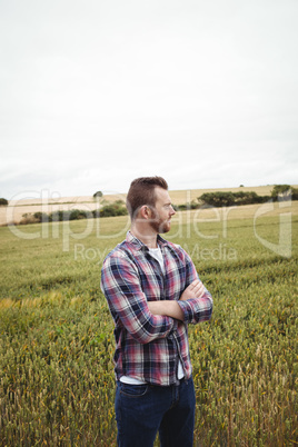 Thoughtful farmer standing with arms crossed in the field