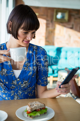 Woman using mobile phone while having coffee