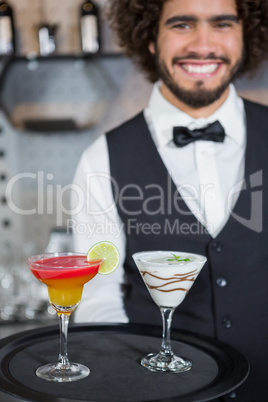 Bartender holding tray of cocktail and milkshake in bar