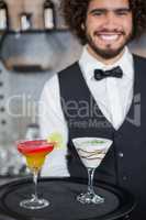 Bartender holding tray of cocktail and milkshake in bar