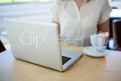 Woman holding a coffee cup and using laptop in coffee shop