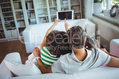 Family sitting on sofa and clicking a selfie on digital tablet