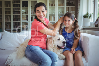 Mother sitting on sofa and tying daughters hair in living room
