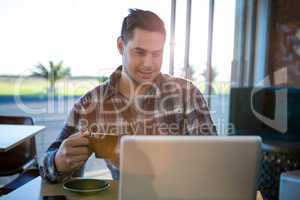 Smiling man using laptop while having coffee