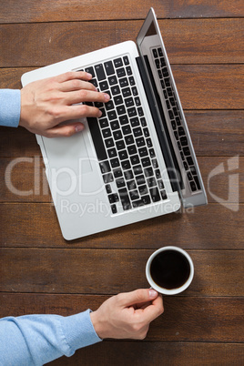 Man using laptop while having cup of coffee