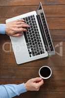 Man using laptop while having cup of coffee