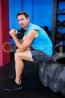 Portrait of serious male athlete sitting on tire