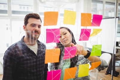 Business people looking at multi colored sticky notes on glass