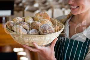 Smiling female staff holding basket of sesame breads at bread counter