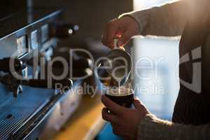 Waiter making cup of coffee at counter in cafe