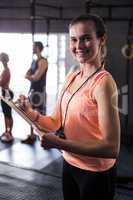 Cheerful female fitness instructor holding clipboard in gym