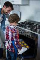 Father and son placing cupcakes tray in oven