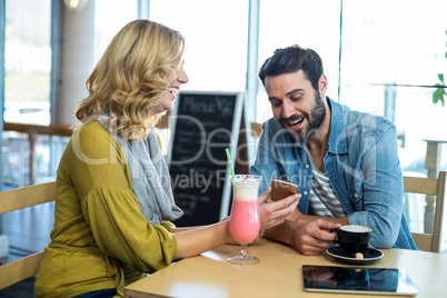 Couple using mobile phone while having a cup of coffee and milkshake