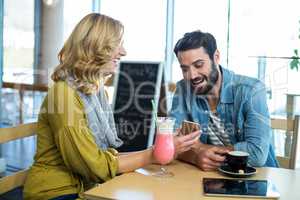 Couple using mobile phone while having a cup of coffee and milkshake