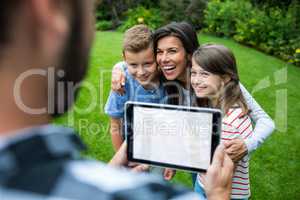 Father clicking picture of family from digital tablet in park