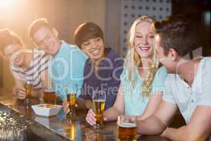 Group of friends interacting with each other while having beer at bar counter