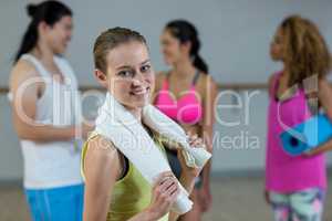 Portrait of female trainer holding towel with fitness class in background