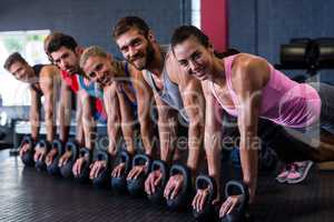 Portrait of smiling friends doing push-ups with kettlebell in gym