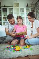 Parents and daughter reading a book while playing with building blocks