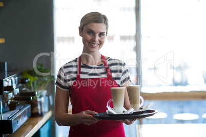 Smiling waitress holding cup of cold coffee at counter in cafe